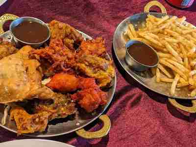 Two plates with Fish Pakora, Chicken Pakora, Veggie Samosa, Onion Bhaji, Veggie Pakora, Fries, Tamarind Sauce